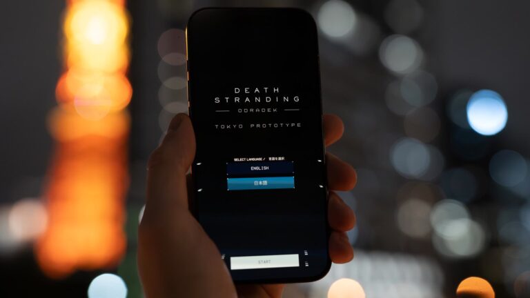 A hand holds a phone showing the Death Stranding Odradek: Tokyo Prototype start screen in front of Tokyo Tower at night